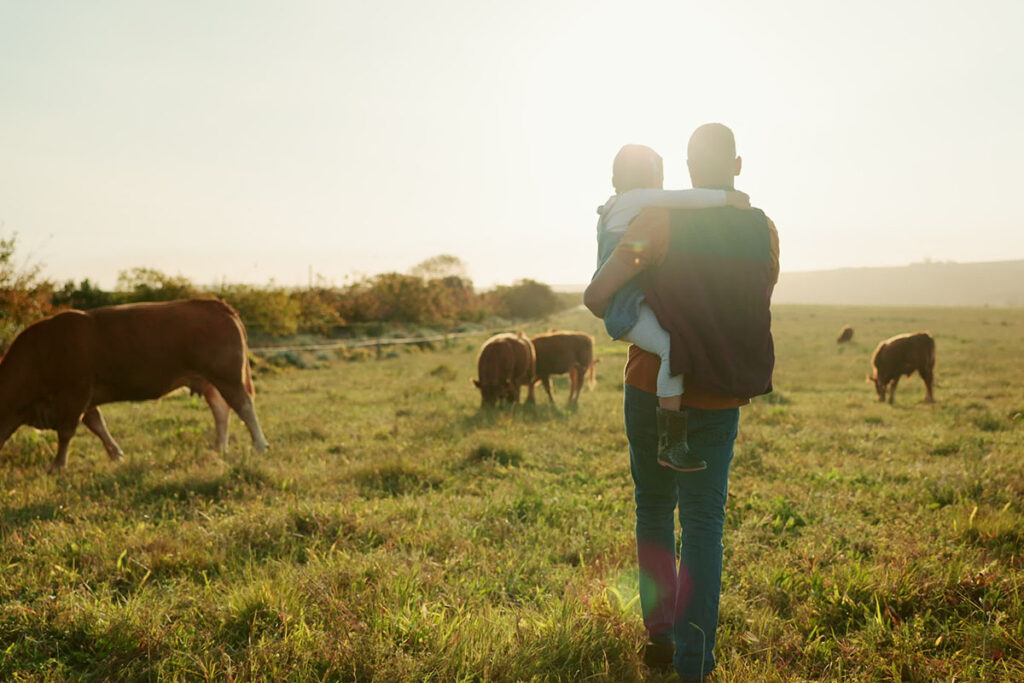 farmer and daughter in a field with a herd of cows